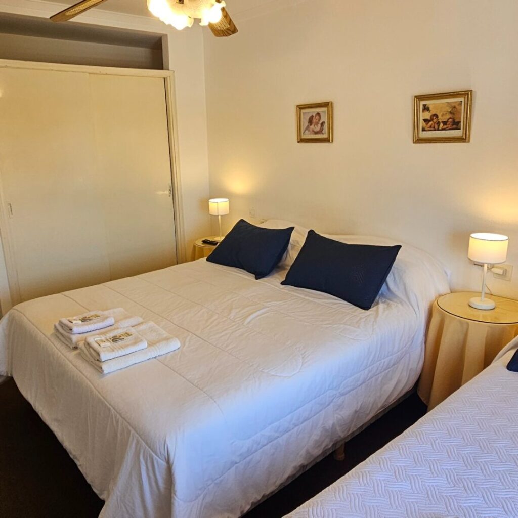 Habitación con cama matrimonial, mesas de luz y balcón al frente